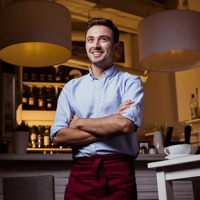 Ein Gastronom steht mit gekreuzten Armen an der Theke einer Bar